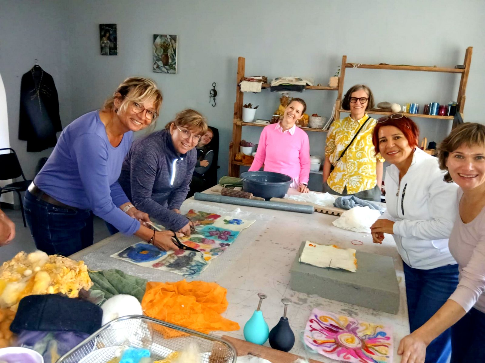 Gruppe von Frauen arbeitet konzentriert und fröhlich an bunten Filzprojekten an einem großen Werkstatttisch, farbige Wollstücke überall