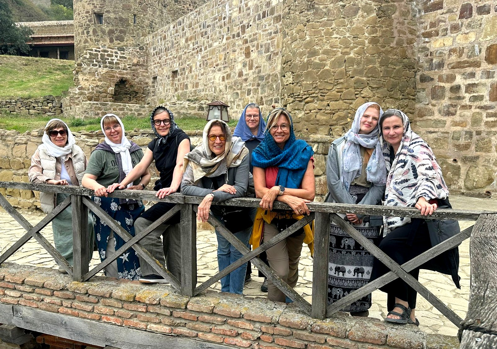 Gruppe von Frauen mit bunten Kopftüchern an einem hölzernen Geländer im Innenhof des Klosters David Gareji, georgische Steinmauern im Hintergrund