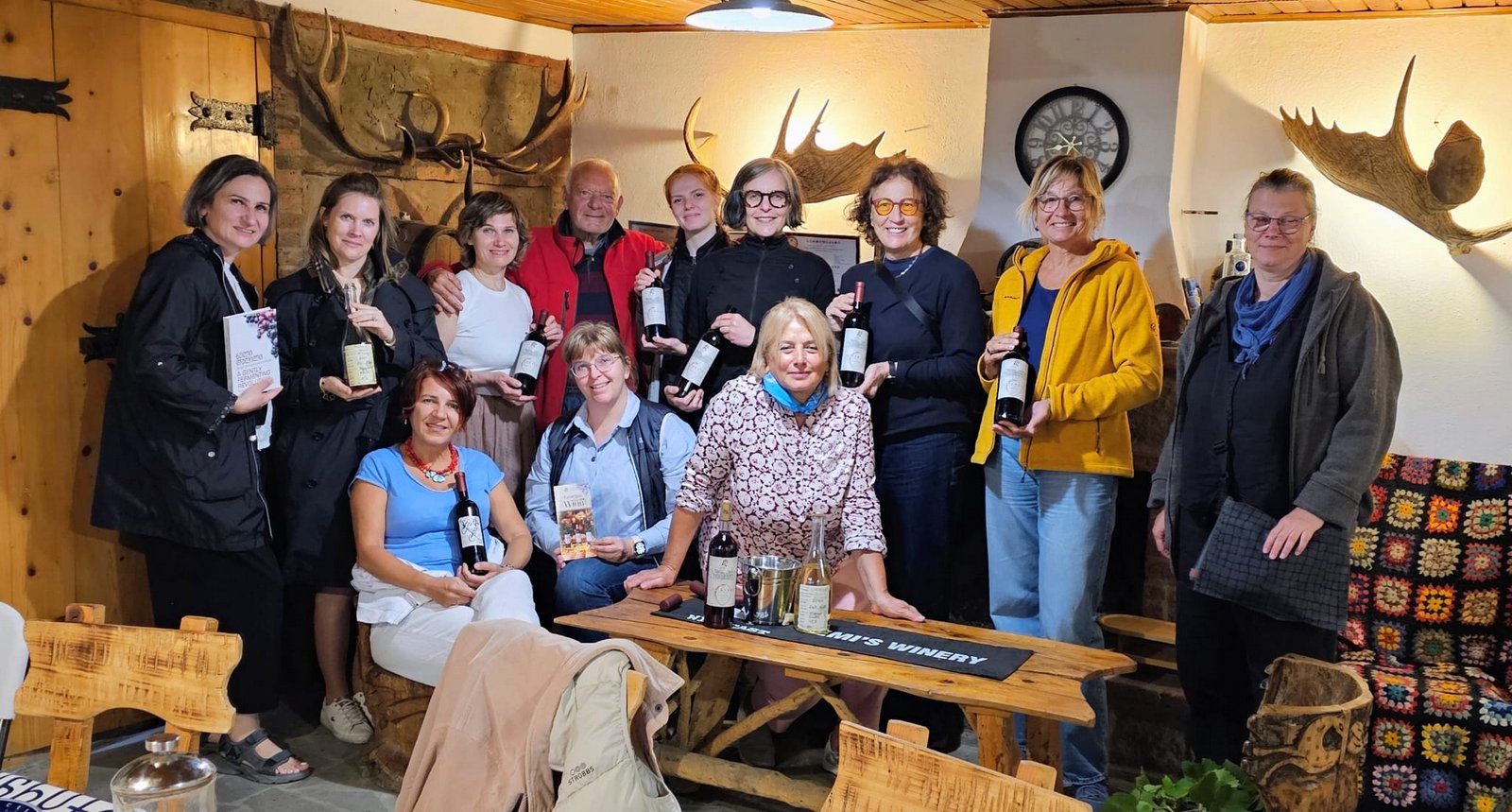 Große Reisegruppe mit Weinflaschen in einem rustikalen Weinkellerraum mit Hirschgeweihen an der Wand und Holzmöbeln, Kaukasus-Reisen Georgien, Chateau Demi