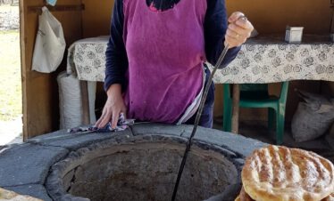 Aserbaidschanische Frau backt traditionelles Fladenbrot an einem runden Tandoor-Steinofen am Straßenrand