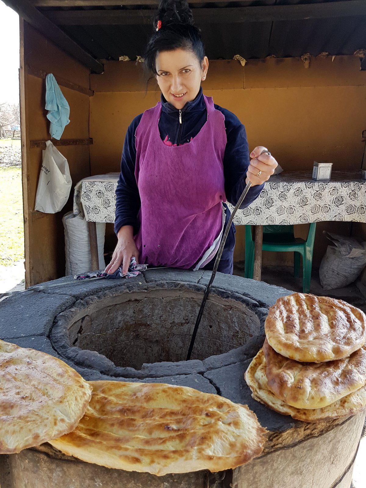 Aserbaidschanische Frau backt traditionelles Fladenbrot an einem runden Tandoor-Steinofen am Straßenrand