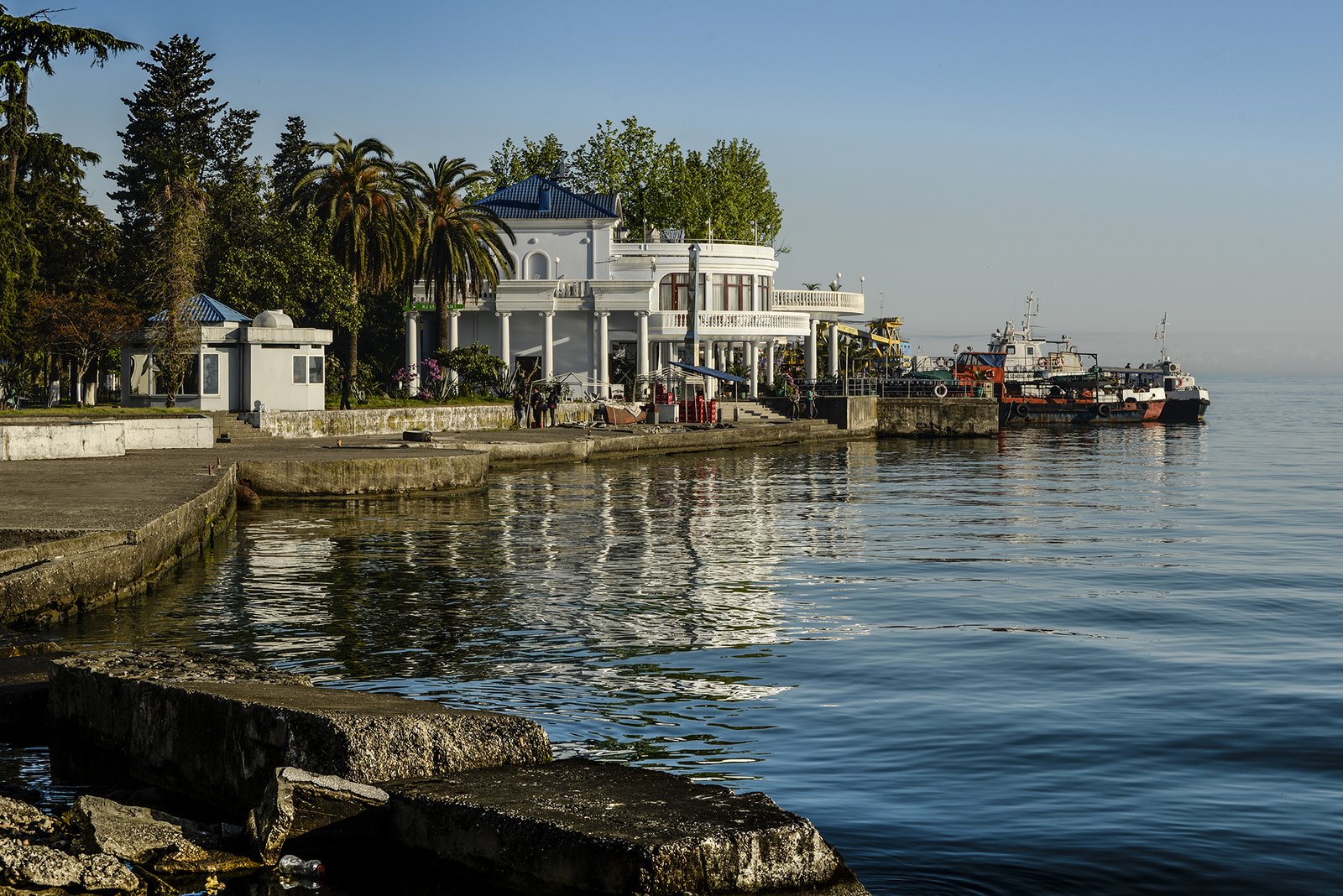 Der Hafen von Batumi am Schwarzen Meer mit einem weißen Kolonialgebäude Palmen und Schiffen im ruhigen Wasser im Morgenlicht