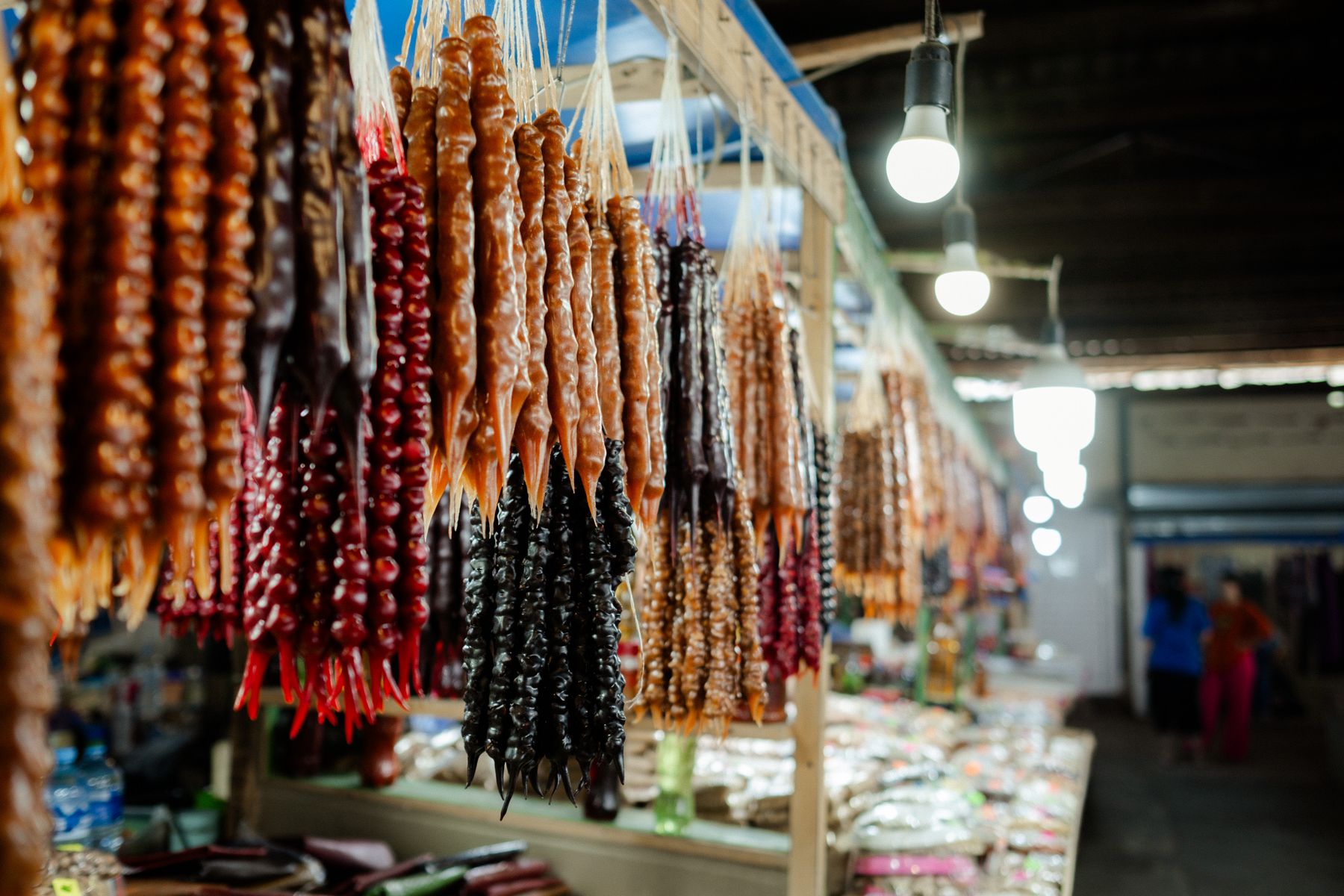 Farbenfrohe Churchkhela (georgische Walnussketten in Traubensaft) hängen an einem Marktstand.