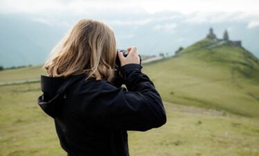 Eine Frau fotografiert die berühmte Gergetier Dreifaltigkeitskirche vor den Kazbek-Gipfeln.