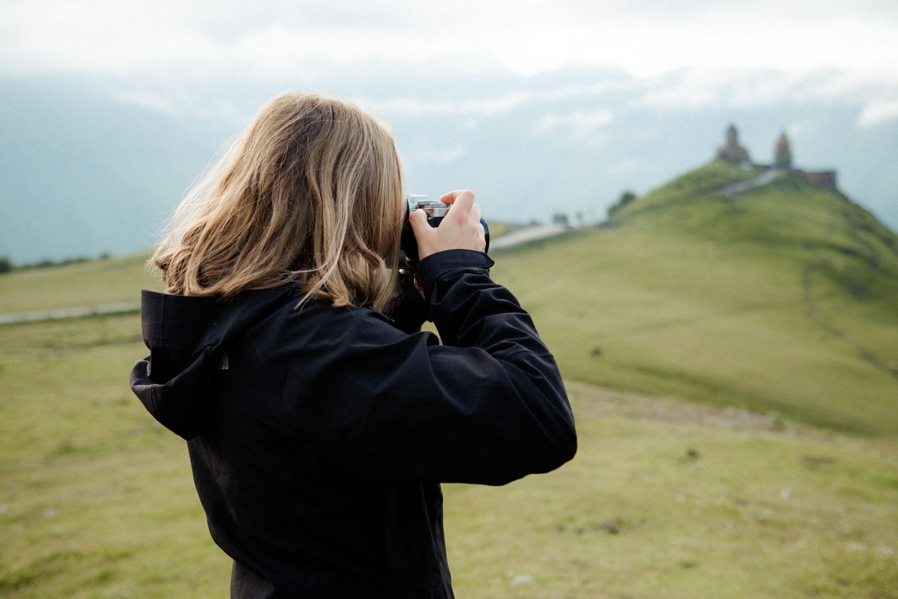 Eine Frau fotografiert die berühmte Gergetier Dreifaltigkeitskirche vor den Kazbek-Gipfeln.