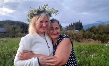 Reiseteilnehmerin und georgische Gastgeberin mit Blumenkranz umarmen sich herzlich.
