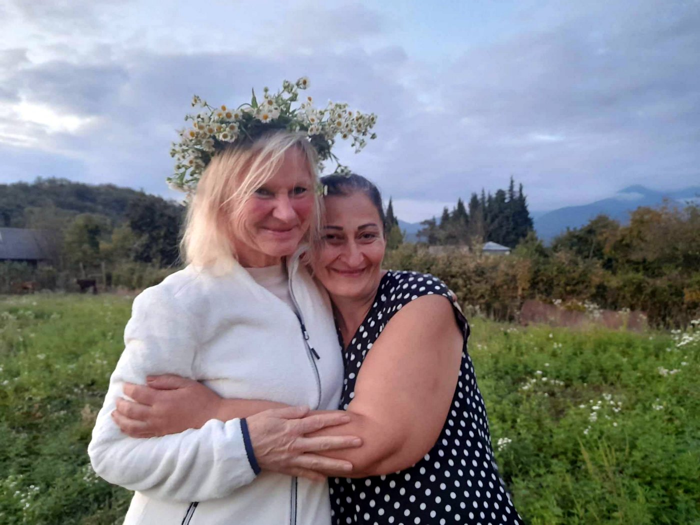 Reiseteilnehmerin und georgische Gastgeberin mit Blumenkranz umarmen sich herzlich.
