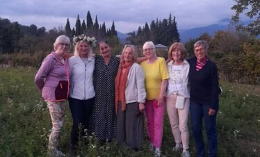 Die Reisegruppe steht Arm in Arm mit ihrer georgischen Gastgeberin auf einer blühenden Wiese.