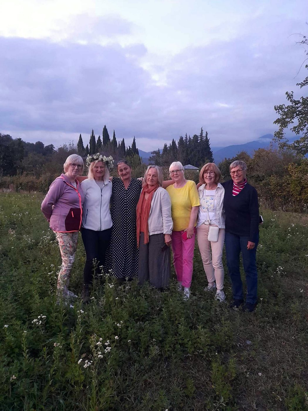 Die Reisegruppe steht Arm in Arm mit ihrer georgischen Gastgeberin auf einer blühenden Wiese.