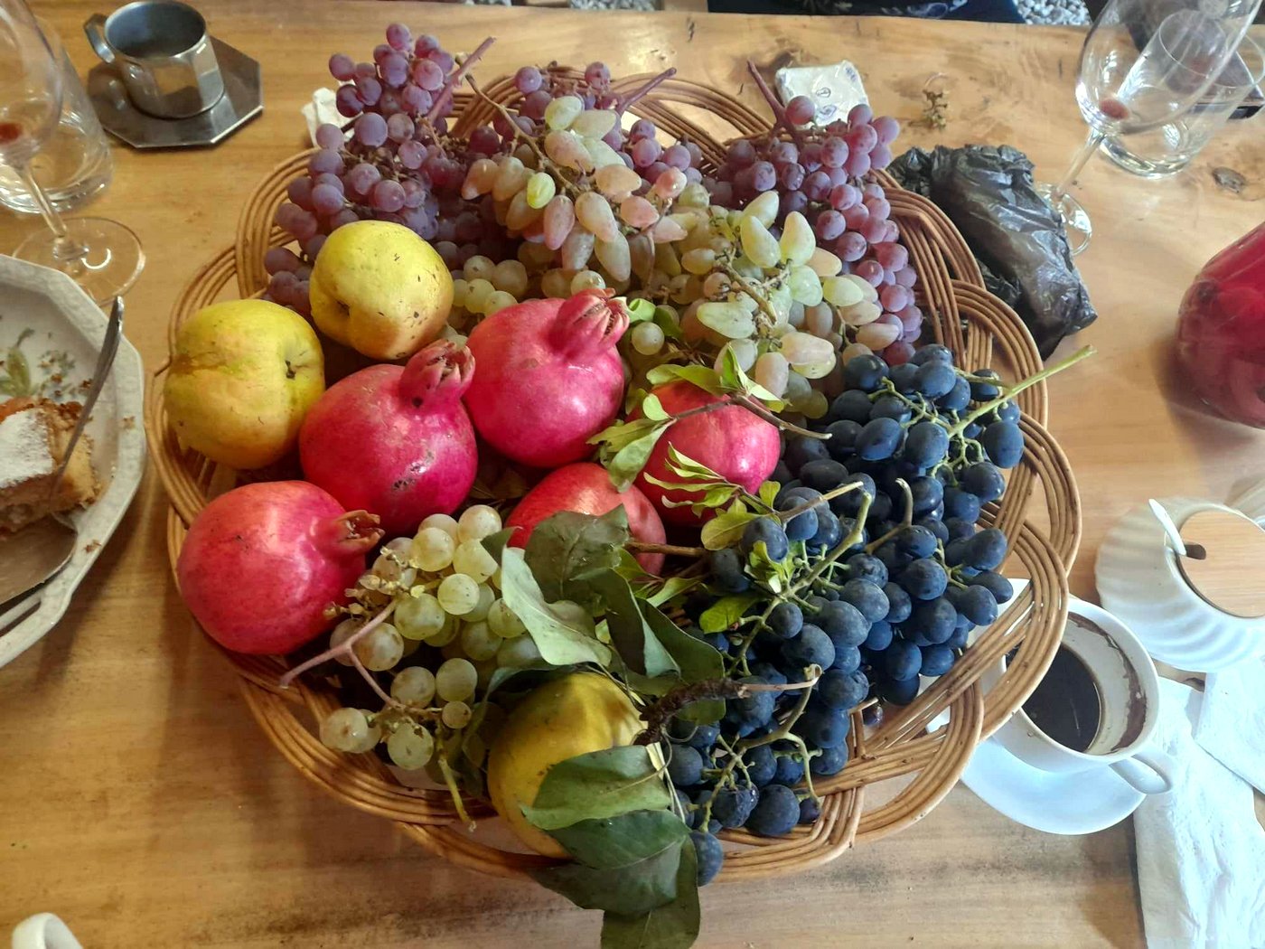 Ein geflochtener Korb voll frischer georgischer Früchte wie Granatäpfel, Weintrauben und Quitten.