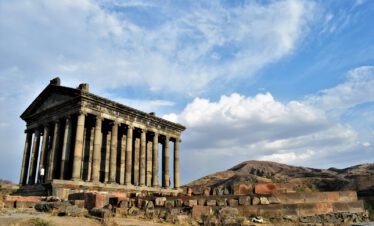 Der griechisch-römische Tempel von Garni in Armenien von unten mit dramatischem Wolkenhimmel und Berge im Hintergrund