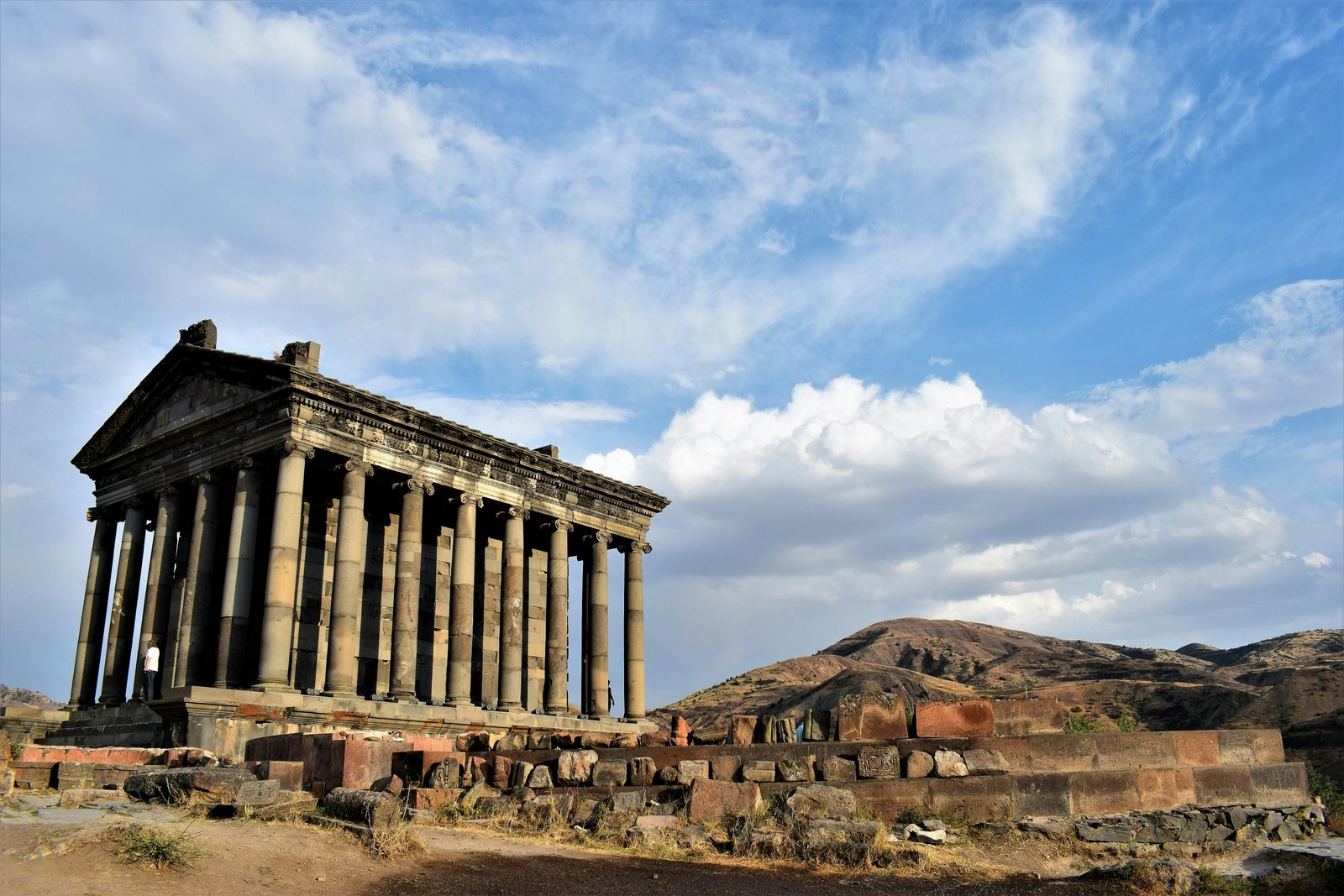 Der griechisch-römische Tempel von Garni in Armenien von unten mit dramatischem Wolkenhimmel und Berge im Hintergrund