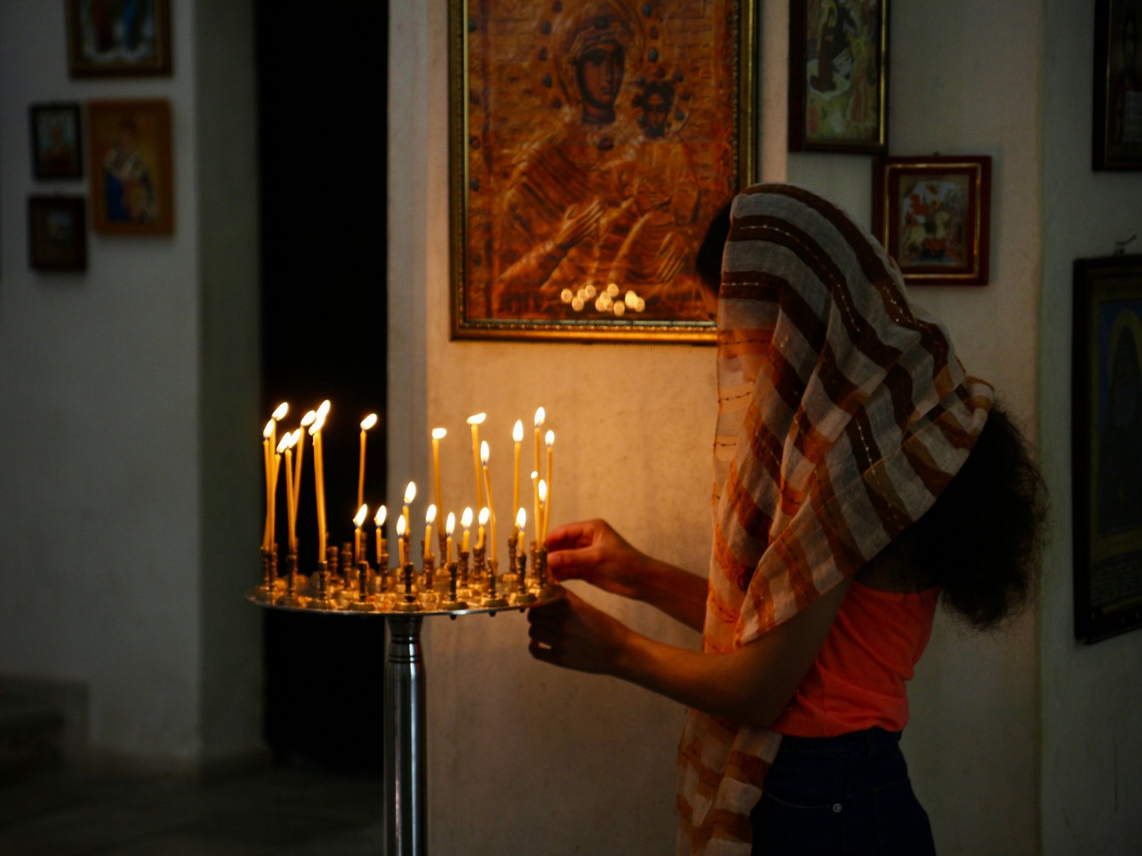 Eine Frau mit Kopftuch zündet Kerzen vor einer Ikone in einer georgisch-orthodoxen Kirche an warmem Kerzenlicht