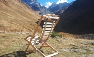 Ein einsamer Holzstuhl blickt ins weite Tschauchi-Tal mit schneebedeckten Gipfeln des Großen Kaukasus bei Dschuta