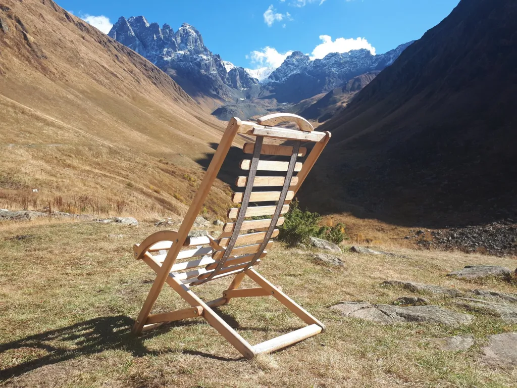 Ein einsamer Holzstuhl blickt ins weite Tschauchi-Tal mit schneebedeckten Gipfeln des Großen Kaukasus bei Dschuta
