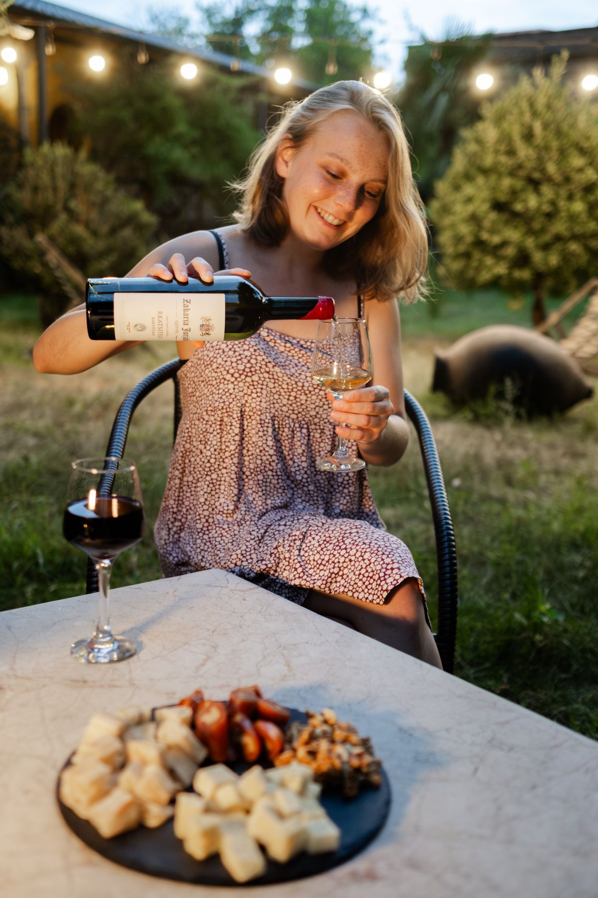 Eine Frau schenkt im warmen Abendlicht georgischen Wein auf einer Terrasse ein.