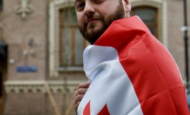 Junger bärtiger Georgier in Tbilissi trägt stolz die georgische Flagge um die Schultern und eine goldene Krone auf dem Kopf