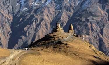 Die Sameba-Gergeti Dreifaltigkeitskirche auf einem Bergrücken vor der massiven Felswand des Kaukasus.