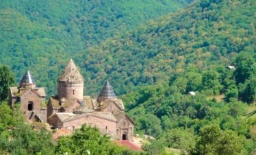 Das mittelalterliche Kloster Goshavank aus rosa Tuffstein mit drei Kirchtürmen eingebettet in dichten grünen Wald bei Dilidjan Armenien