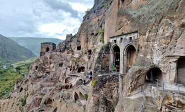 Blick auf die in den Fels gehauenen Höhlen, Treppen und Bogengänge der mittelalterlichen Höhlenstadt Wardsia im grünen Canyon des Mtkwari-Flusses in Südgeorgien