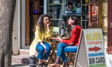 Zwei junge Frauen sitzen an einem Außentisch eines Cafés in Jerewan Armenien mit Weinflaschen und georgischer Schrift im Hintergrund
