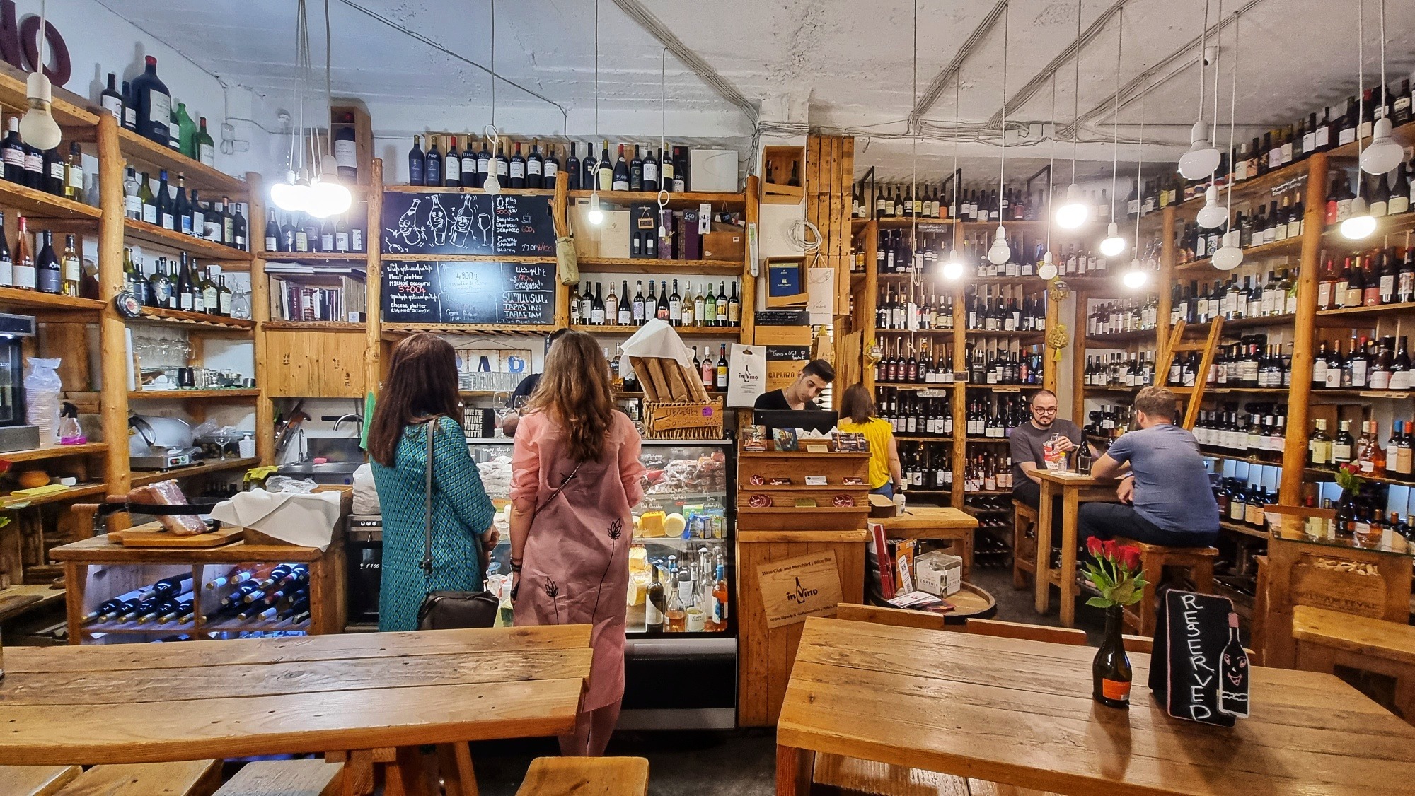 Rustikale Weinbar In Vino in Jerewan Armenien mit Holzregalen voller Weinflaschen und Gästen an Tischen