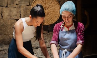 Zwei Frauen bereiten gemeinsam traditionelle georgische Khinkali Teigtaschen an einem Holztisch zu.