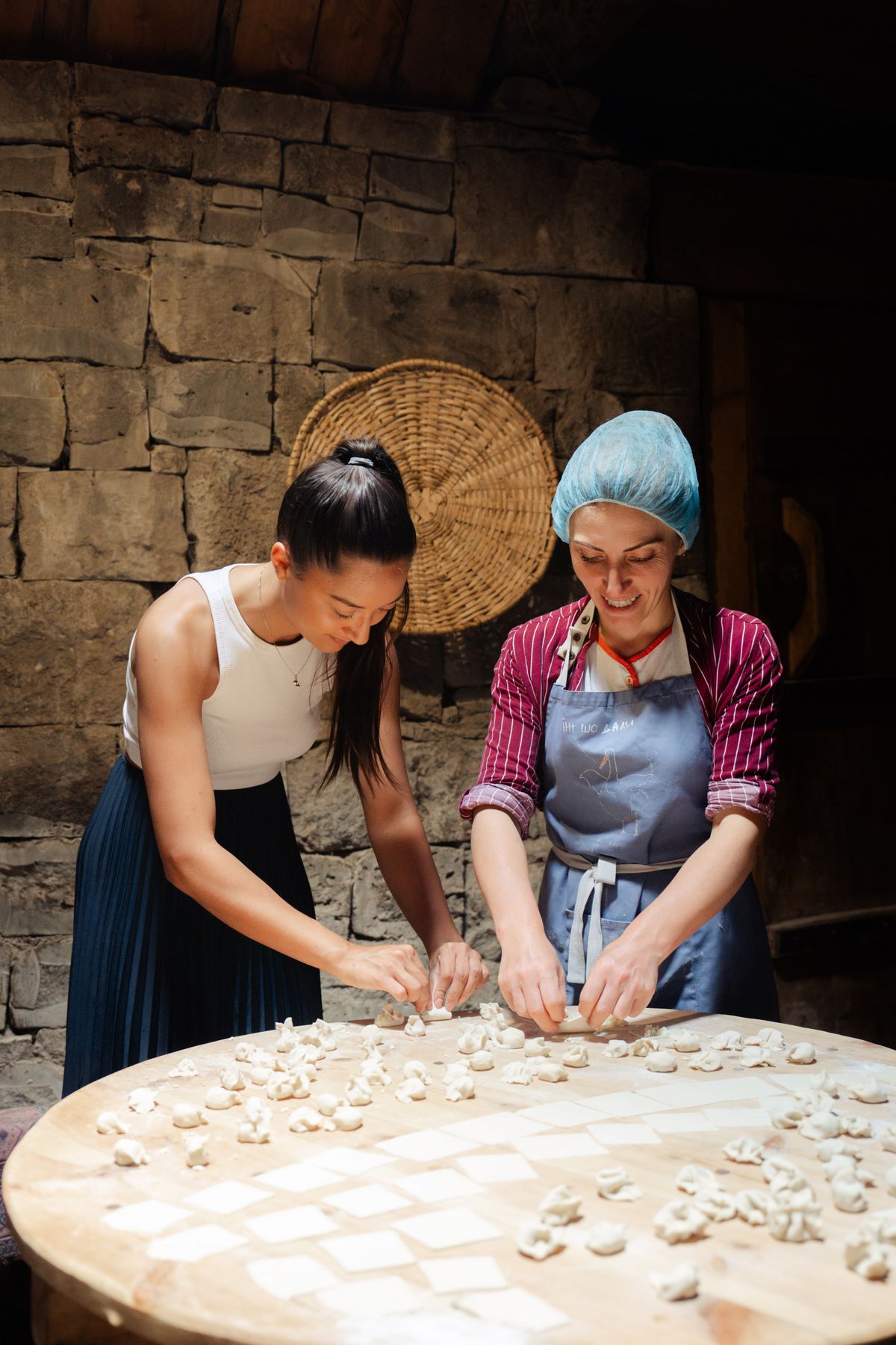 Zwei Frauen bereiten gemeinsam traditionelle georgische Khinkali Teigtaschen an einem Holztisch zu.