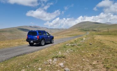 Blauer Nissan Xterra 4x4 mit Kaukasus-Reisen Logo auf einer Straße der armenischen Hochebene mit weiten Hügeln und blauem Himmel