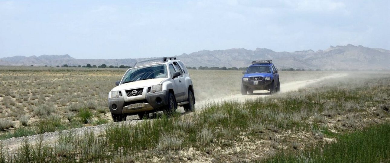 Zwei Nissan Xterra Mietwagen fahren auf einer Schotterpiste durch die weite Steppe in Georgien.