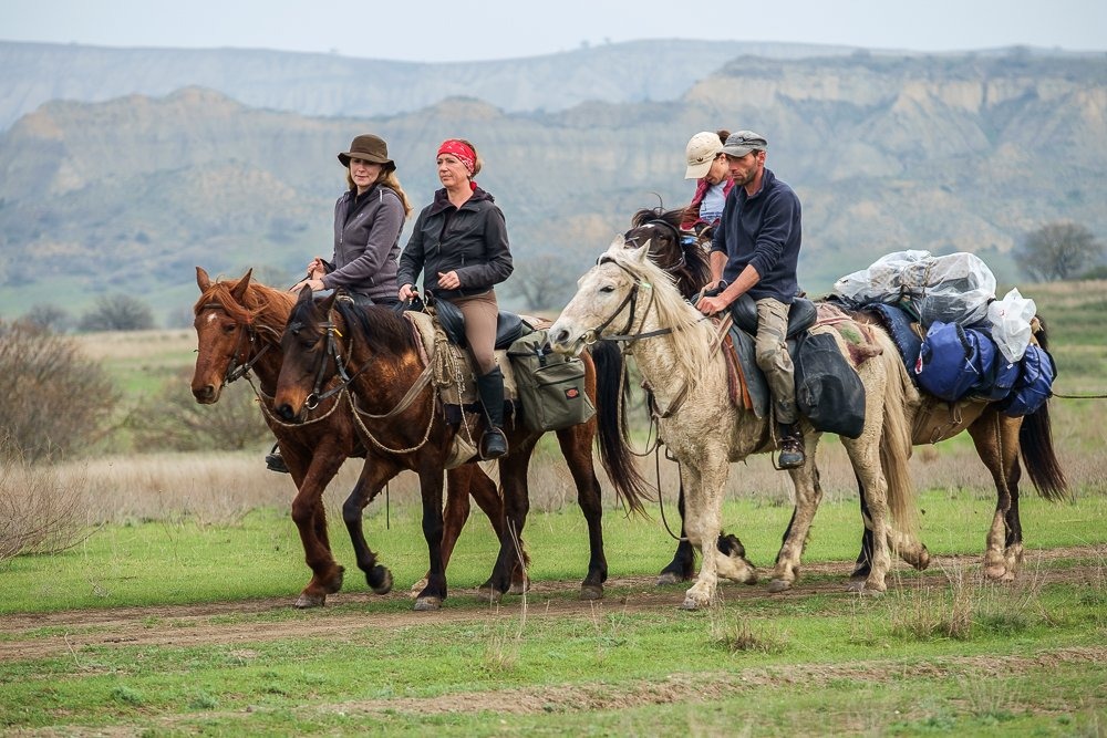 Reitergruppe auf tuschetischen Pferden vor den markanten Sandstein-Tafelbergen des Nationalparks Vashlovani, Georgien