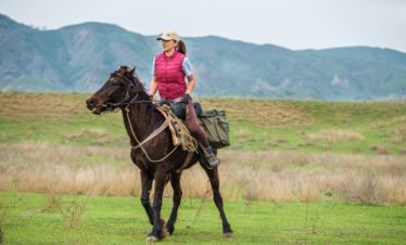 Reiterin auf schwarzem tuschetischen Pferd in der weiten Steppenlandschaft des Nationalparks Vashlovani vor dem Kaukasus