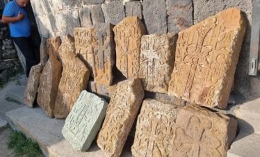 Mehrere armenische Khachkare aus orangefarbenem Tuffstein mit filigranen Kreuzornamenten am Kloster Sevanavank