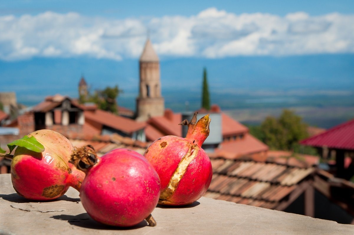 Reife rote Granatäpfel auf einer Steinmauer vor dem Panorama der Stadt Sighnaghi in Georgien.