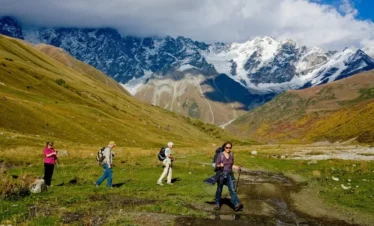 Aktive Wandergruppe mit Rucksäcken auf einem Pfad im Hochgebirge von Swanetien vor schneebedeckten Gipfeln.