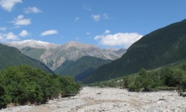 Weites Flusstal mit Kiesbett und schneebedeckten Gipfeln im Großen Kaukasus, Aserbaidschan
