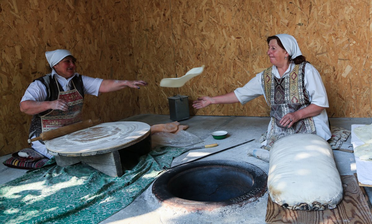 Zwei armenische Frauen in Tracht backen gemeinsam Lavash-Brot am traditionellen Tonir-Ofen