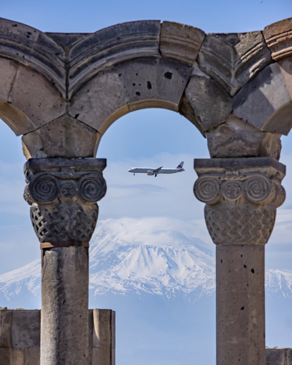 Steinerne Säulen der Ruinen von Zvartnots mit einem Flugzeug und dem schneebedeckten Ararat im Hintergrund, Armenien