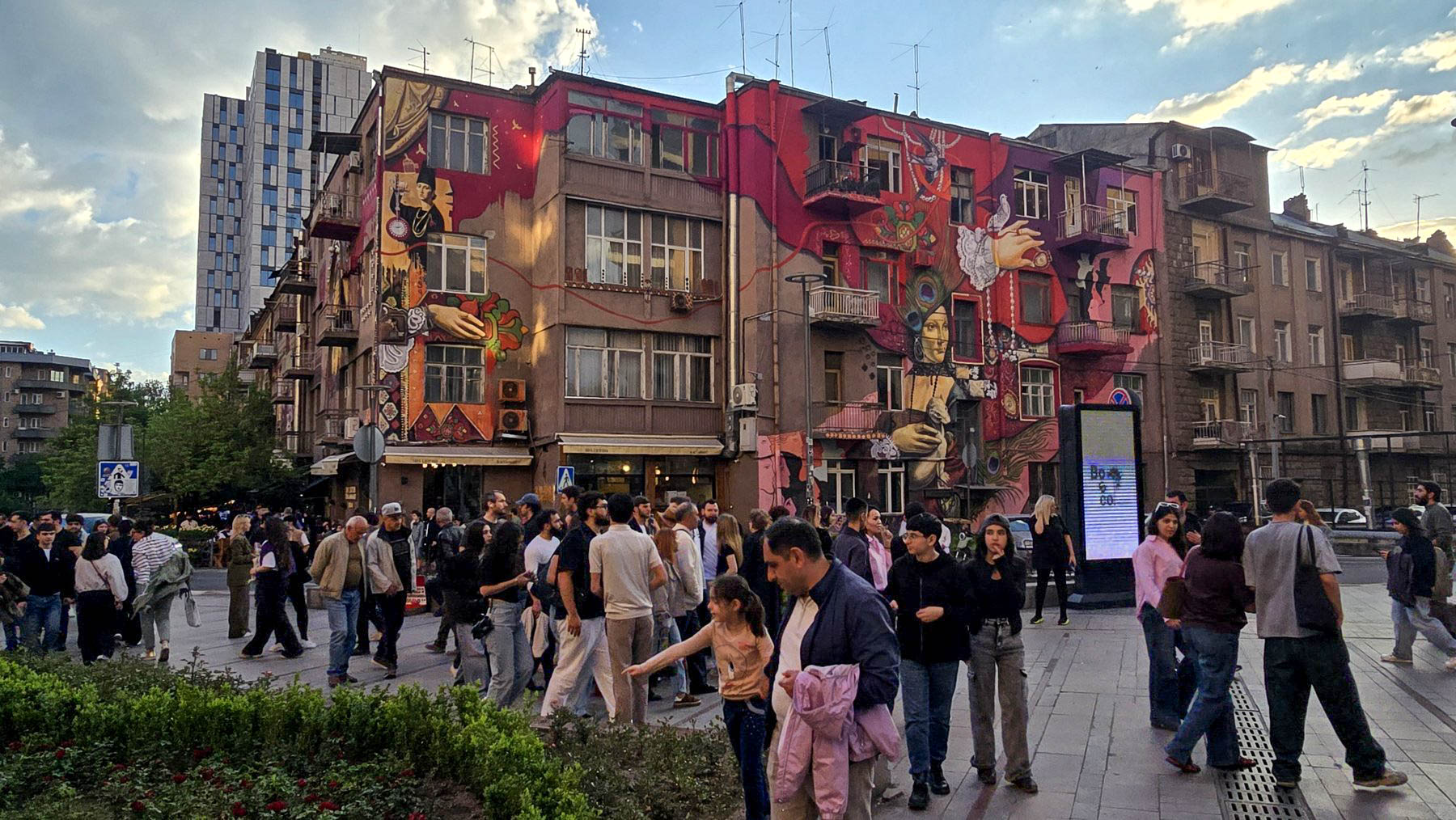 Busy evening street scene in central Yerevan with murals and pedestrians